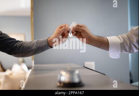 L'hôtesse d'accueil de l'hôtel est méconnaissable et donne la clé au client à la réception, en gros plan Banque D'Images
