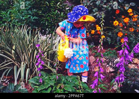 Fille enfant en robe florale fleurs d'eau dans le jardin avec un arrosoir en plastique Banque D'Images