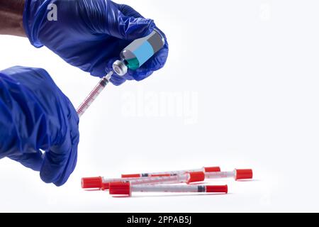 Main du médecin dans des gants bleus tenant une seringue avec un flacon de vaccin vert, une seringue couchée. Banque D'Images