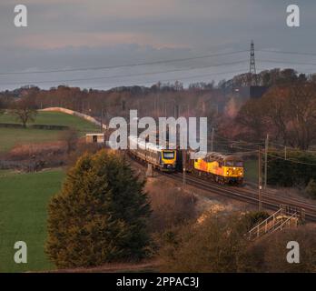 Colas Railfreight classe 56 locomotivestracing d'un long train de marchandises transportant du bois sur la ligne principale de la côte ouest passant par un train de voyageurs Northern Rail Banque D'Images