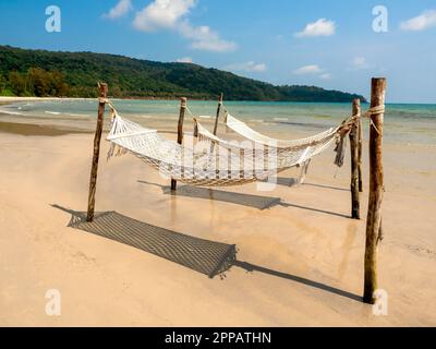 Deux berceau de corde vide suspendu sur les poteaux en bois sur la plage de sable sur la mer, l'île et le fond bleu ciel. Berceau suspendu ou lit pliant pour deux personnes Banque D'Images