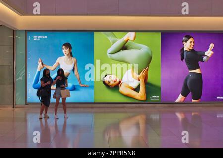 Les amateurs de shopping à ION Orchard (centre commercial) sur Orchard Rd, à Singapour, passent devant de grandes publicités sur le thème du yoga pour la société « Luclulemon » qui vend des vêtements de sport Banque D'Images