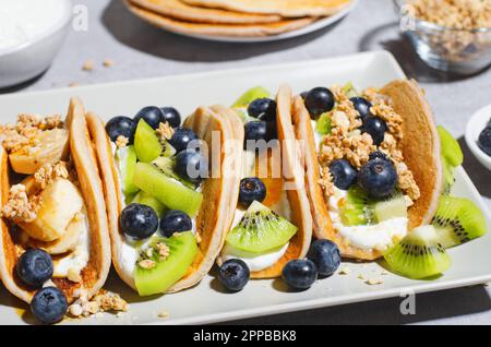 Crêpes Taco avec fruits frais, bleuets et yaourt, petit déjeuner sain ou en-cas sur fond lumineux Banque D'Images