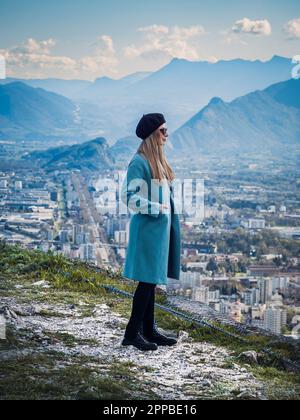 Jeune belle femme debout sur une colline surplombant la magnifique ligne d'horizon de la ville de Grenoble et des montagnes environnantes des Alpes françaises Banque D'Images