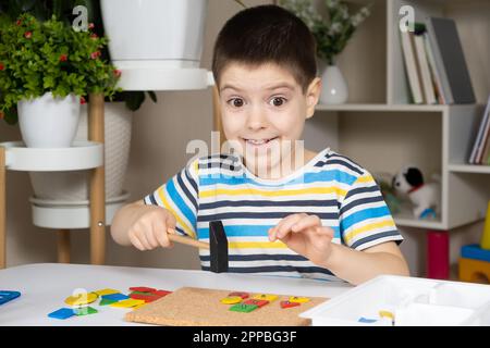 Un enfant d'âge préscolaire joue avec une mosaïque, construit des figures sur une planche, martelant des ongles avec un marteau sur des parties multicolores du concepteur Banque D'Images