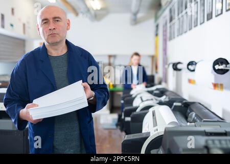 Portrait d'un employé de la maison d'impression avec pile de papier dans ses mains Banque D'Images