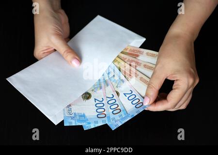 Enveloppe avec roubles russes dans les mains des femmes sur fond noir. Salaires en Russie, concept de bonus ou de pot-de-vin Banque D'Images
