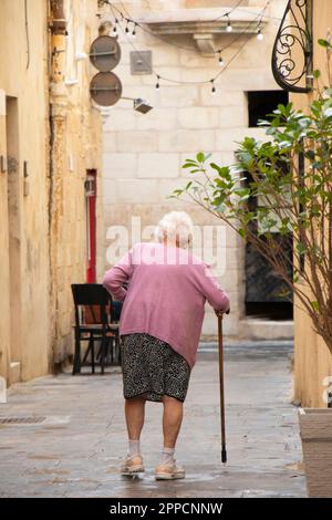 Rabat, Malte - 13 novembre 2022: Femme super senior marchant avec une canne dans la rue piétonne, de l'arrière Banque D'Images