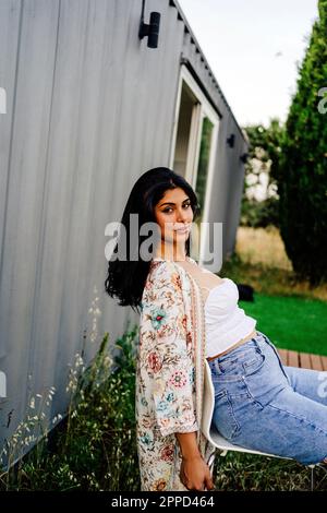 Jeune femme assise sur une chaise à l'extérieur de la maison du conteneur Banque D'Images