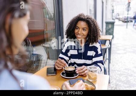 Jeune femme souriante assise avec un ami au café-terrasse Banque D'Images