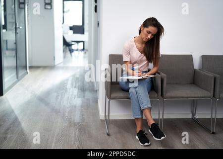 Femme remplissant la forme assis dans la salle d'attente Banque D'Images