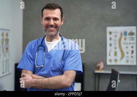Sourire un médecin mûr debout avec les bras croisés en clinique Banque D'Images