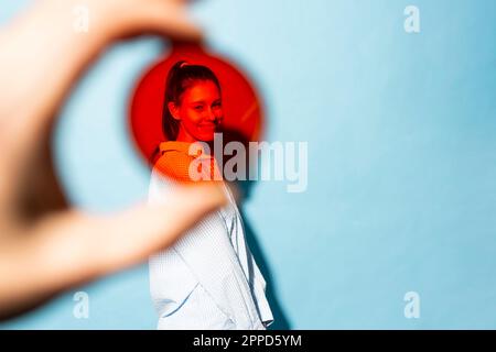 Jeune femme souriante vue à travers le filtre de lentille rouge sur fond bleu Banque D'Images
