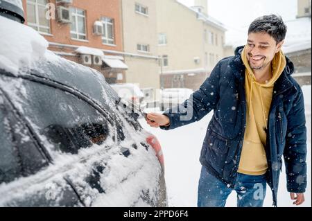 Un homme heureux qui retire la neige de la voiture à l'aide d'une brosse Banque D'Images