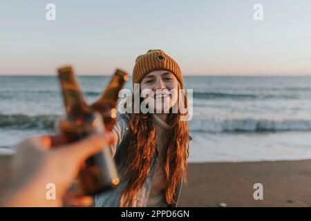 Bonne femme toaster la bouteille de bière avec un ami en face de la mer Banque D'Images