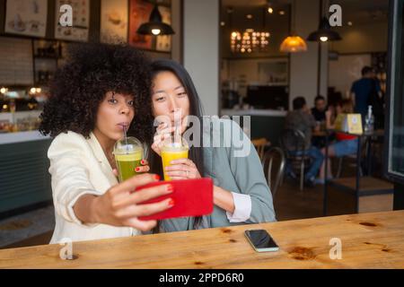 Des amis qui prennent du selfie en buvant du jus sain au café Banque D'Images