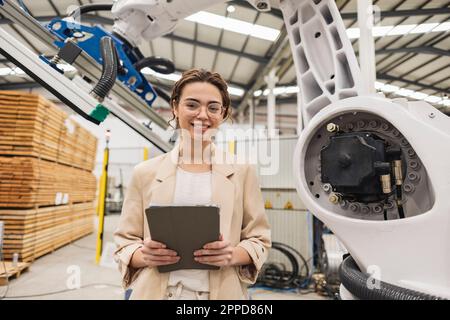 Ingénieur souriant debout avec une tablette PC devant le bras robotique Banque D'Images
