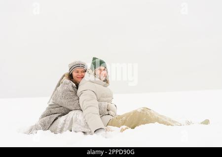 Femme embrassant un ami du dos assis dans la neige Banque D'Images