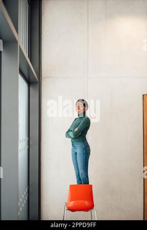 Jeune femme aux bras croisés debout sur la chaise Banque D'Images