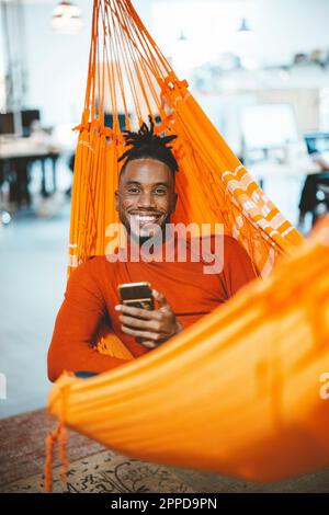 Un jeune homme d'affaires heureux se détendant dans un hamac avec un smartphone au bureau Banque D'Images