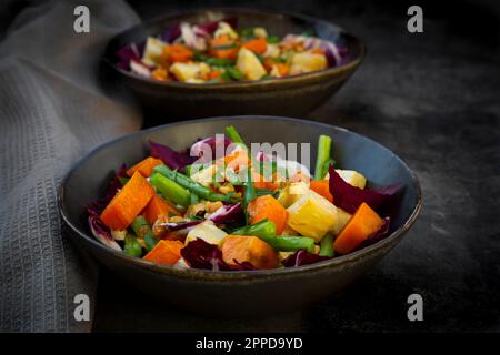 Deux bols de salade végétarienne prête à consommer avec patate douce, céleri, radicchio, haricots verts, croûtons, noix et persil Banque D'Images