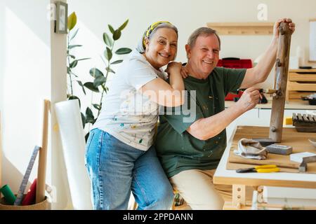 Bonne femme âgée avec main sur l'épaule sur l'homme appliquant du vernis sur le bois dans l'atelier Banque D'Images