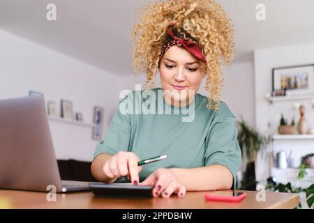Jeune femme souriante utilisant une calculatrice avec un ordinateur portable au bureau Banque D'Images