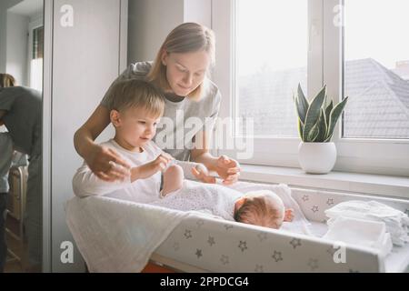 Femme et garçon qui s'occupe de bébé dormant sur une table à langer à la maison Banque D'Images