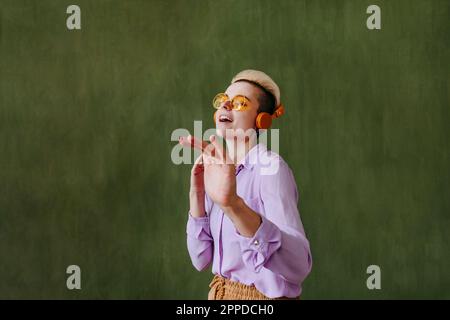 Une jeune femme insouciante portant des lunettes de soleil en train de danser devant le mur vert Banque D'Images