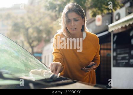 Femme inquiète de ramasser un chiffon sale sur le pare-brise de la voiture Banque D'Images