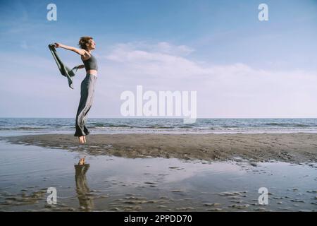 Femme insouciante aux bras débordés sautant à la plage Banque D'Images