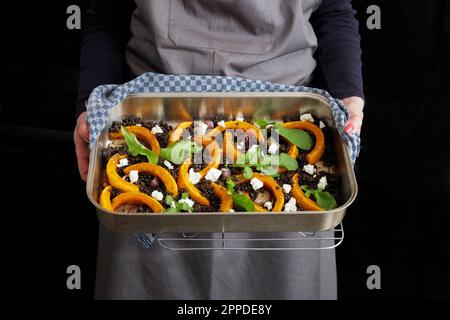 Femme tenant une plaque de cuisson avec des citrouilles grillées, de la betterave commune, du fromage feta et de l'arugula Banque D'Images