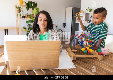 Mère travaillant sur un ordinateur portable pendant que le garçon joue à table Banque D'Images
