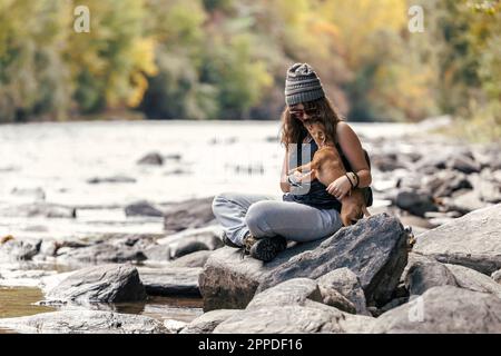 Fille jouant avec un chien assis à pieds croisés sur le rocher près de la rivière Banque D'Images