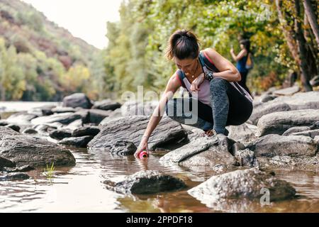 La mère s'accrousse sur la roche remplissant la bouteille d'eau de la rivière Banque D'Images