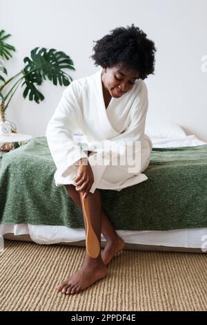 Femme massant la jambe avec une brosse dans la chambre à la maison Banque D'Images