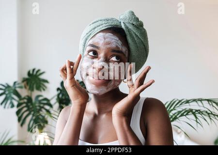 Jeune femme portant une serviette sur la tête et appliquant un masque facial à la maison Banque D'Images