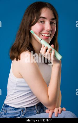 Happy Teenage Girl tenant la brosse à dents électrique assis | fond bleu Banque D'Images