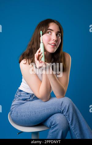 Happy Teenage Girl tenant la brosse à dents électrique assis | fond bleu Banque D'Images