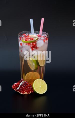 Un grand verre de limonade rafraîchissante avec des graines de grenade et de la glace sur fond noir, à côté de fruits mûrs. Disposition verticale. Banque D'Images