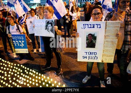 Tel Aviv, Israël. 22nd avril 2023. Les membres de la famille endeuillée tiennent des pancartes avec des photos de leurs proches, à côté de milliers de bougies « Yom Hazikaron » pour le jour du souvenir des soldats israéliens tombés et des attaques terroristes contre les victimes lors d'une manifestation de révision judiciaire à tel Aviv. Crédit : SOPA Images Limited/Alamy Live News Banque D'Images