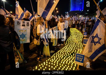 Tel Aviv, Israël. 22nd avril 2023. Les membres de la famille endeuillée tiennent des pancartes avec des photos de leurs proches, à côté de milliers de bougies « Yom Hazikaron » pour le jour du souvenir des soldats israéliens tombés et des attaques terroristes contre les victimes lors d'une manifestation de révision judiciaire à tel Aviv. Crédit : SOPA Images Limited/Alamy Live News Banque D'Images