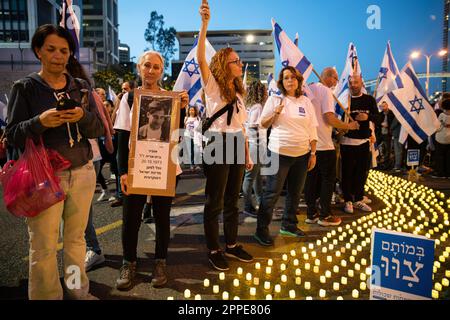 Tel Aviv, Israël. 22nd avril 2023. Les membres de la famille endeuillée tiennent des pancartes avec des photos de leurs proches, à côté de milliers de bougies « Yom Hazikaron » pour le jour du souvenir des soldats israéliens tombés et des attaques terroristes contre les victimes lors d'une manifestation de révision judiciaire à tel Aviv. Crédit : SOPA Images Limited/Alamy Live News Banque D'Images