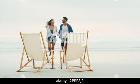 Asseyez-vous une seconde. Prise de vue en longueur d'un jeune couple affectueux marchant vers un ensemble de chaises de plage pendant la journée. Banque D'Images