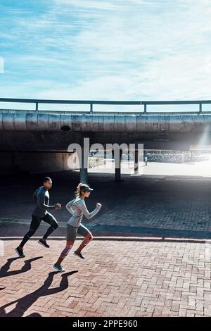 Rester en forme ensemble. Prise de vue en longueur de deux jeunes et jeunes sportifs qui traversent la ville. Banque D'Images