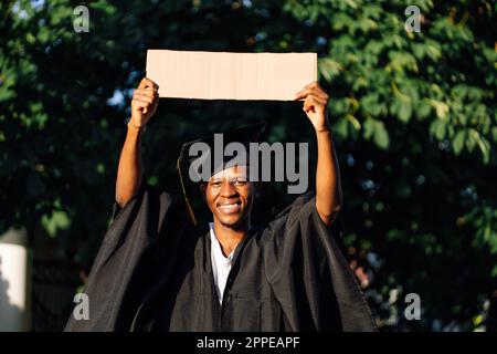 Portrait d'un homme noir souriant debout avec une affiche en carton vide surélevée dans la rue à la recherche d'un travail, espace de copie libre. Université ou collège Banque D'Images