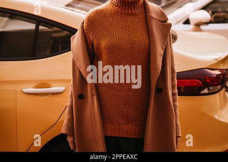 Corps féminin dans le pull chaud orange confortable et long manteau brun contre le taxi jaune. Vêtements d'automne urbains style rue concept Banque D'Images