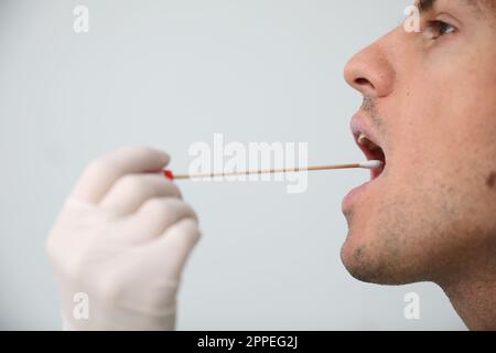 Médecin prenant l'échantillon pour le test d'ADN de l'homme sur fond clair, gros plan Banque D'Images