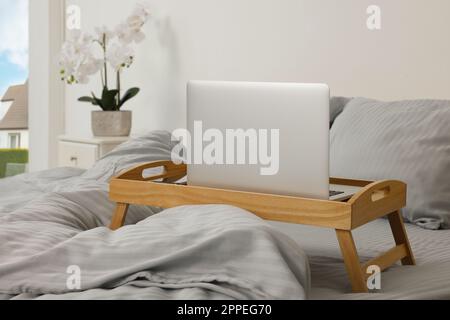Plateau table en bois avec ordinateur portable et smartphone sur le lit à l'intérieur Banque D'Images