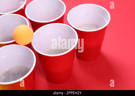 Tasses en plastique et balle pour bière-pong sur fond rouge Banque D'Images